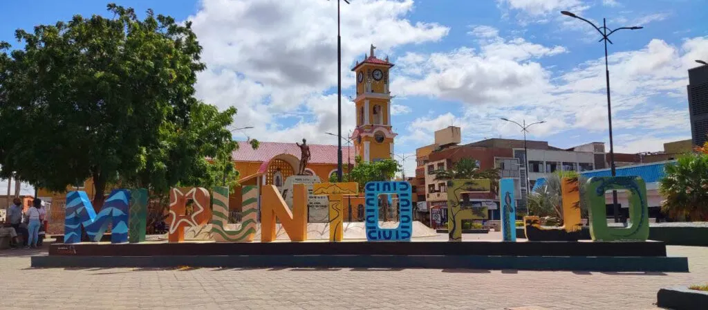 Las letras de colores de PUNTO FIJO en la plaza, con la iglesia y su torre del reloj detrás, bajo un cielo azul.